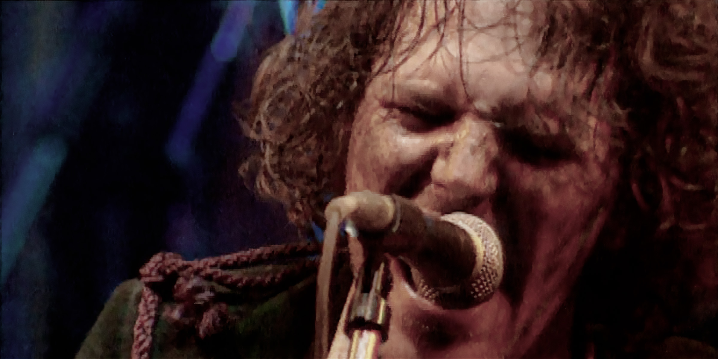 Close up photo of Tim Smith of Cardiacs from live video, singing on microphone